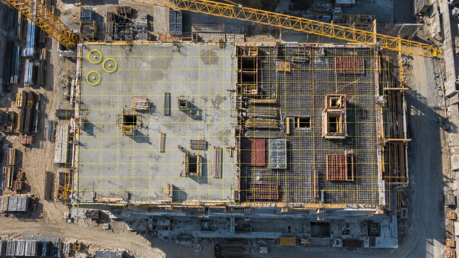 Top-down drone view at midday of a concrete building frame, with a fine yellow grid covering the whole top slab and three small circles marking spot checks in one corner
