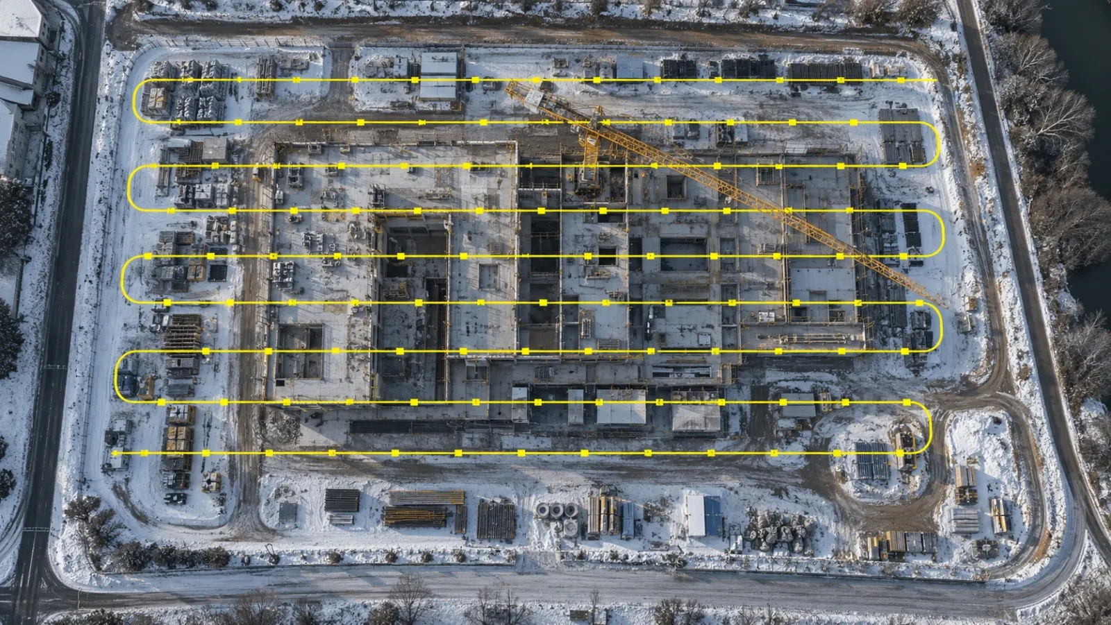 Top-down drone view of a snowy construction site with a yellow flight path of parallel lines and capture points covering it